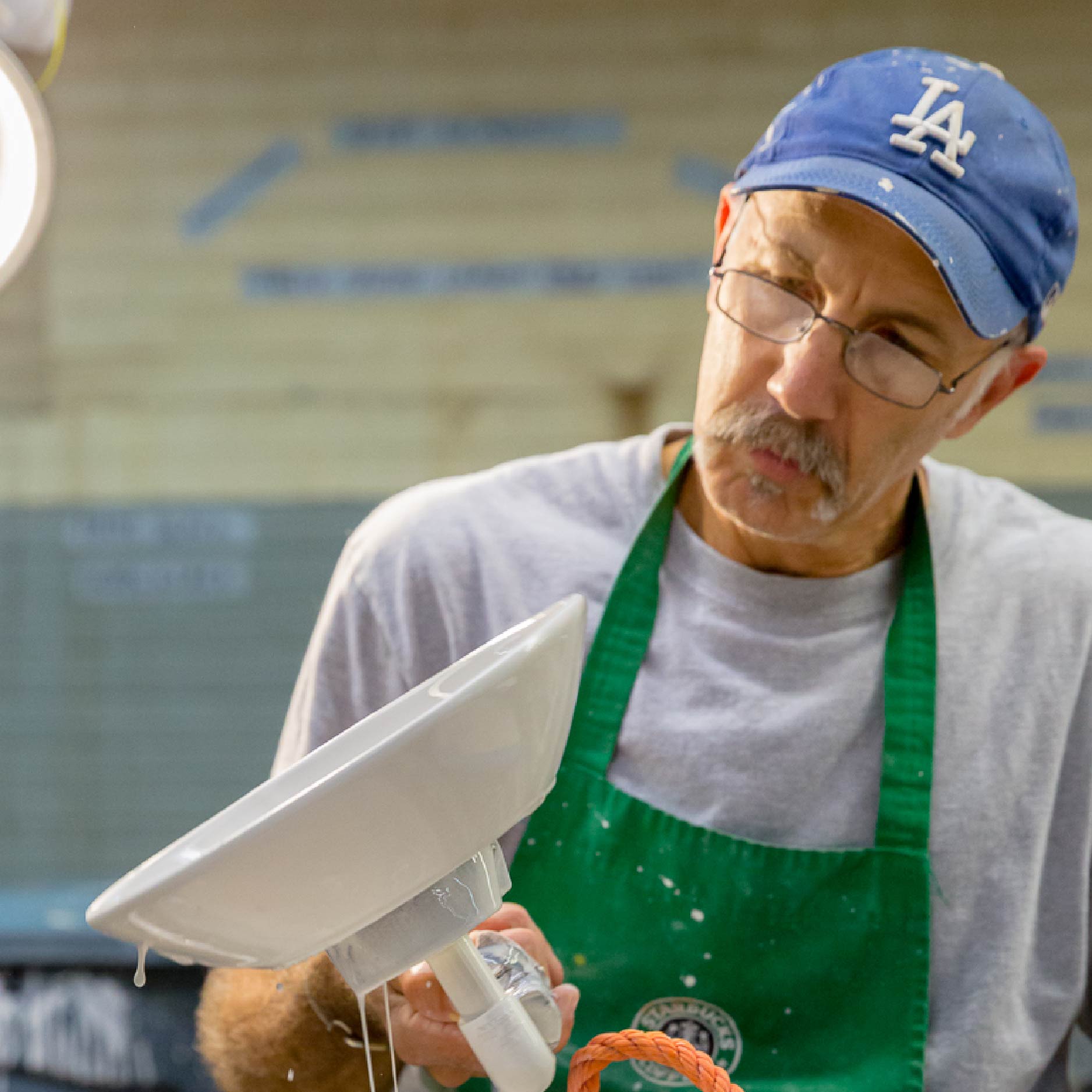 A glazer holds a bowl as the glaze drips off of it