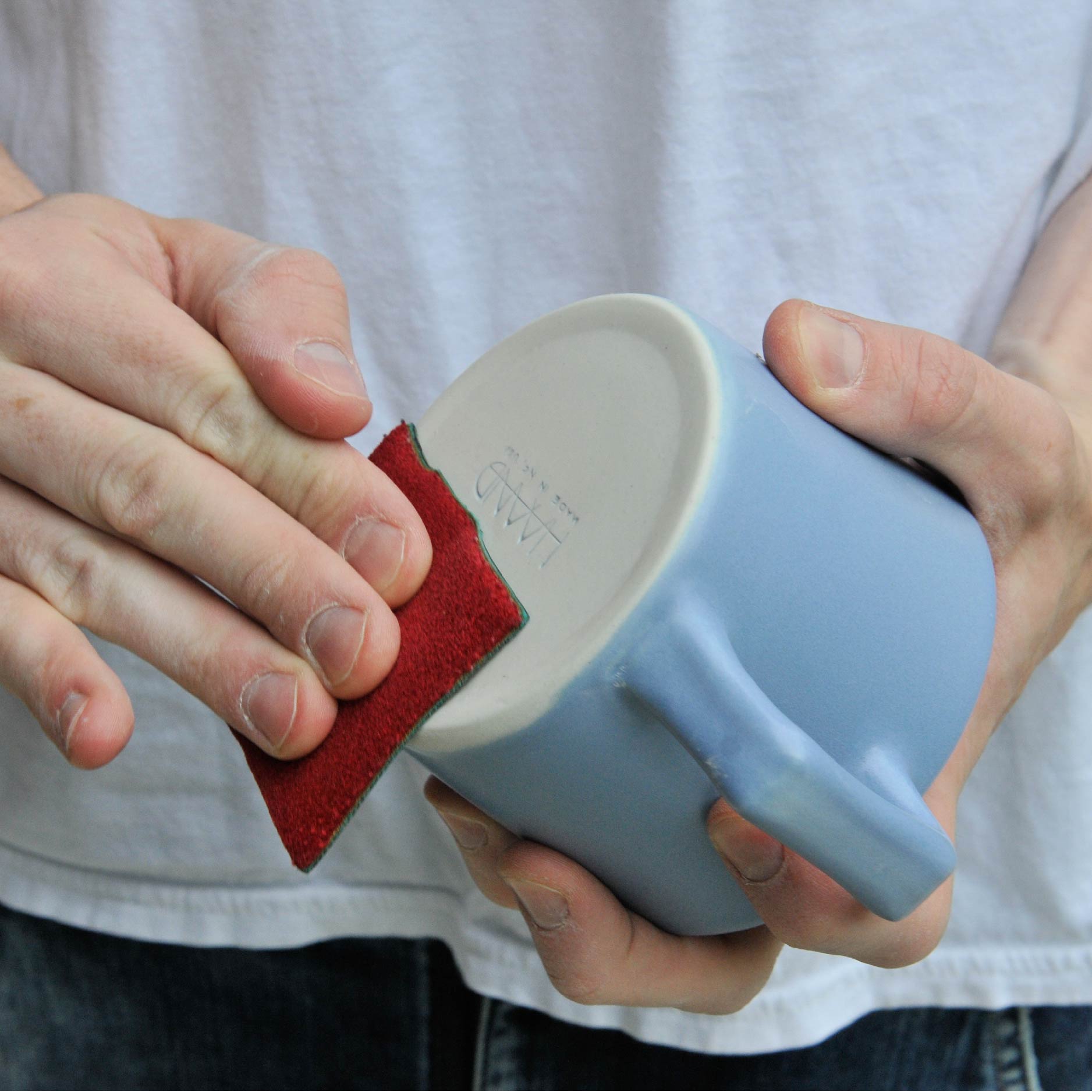 A hand polishes the bottom of a blue mug